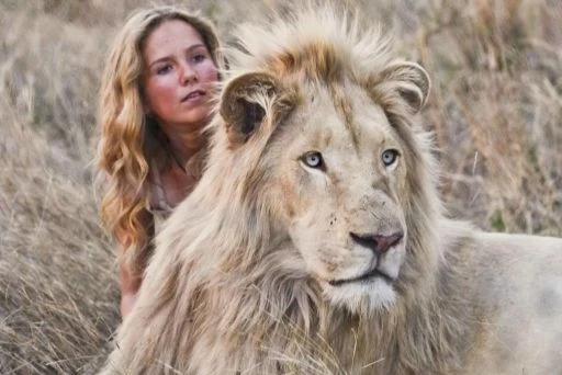 Bílý lev stojí v trávě vedle ženy.