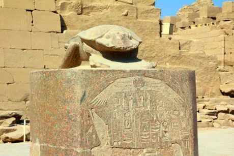 Kámen s egyptským skarabeem na podstavci před starobylými zbytky.