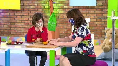 Žena s dítětem sedí u stolu v interiéru před cihlovou zdí.