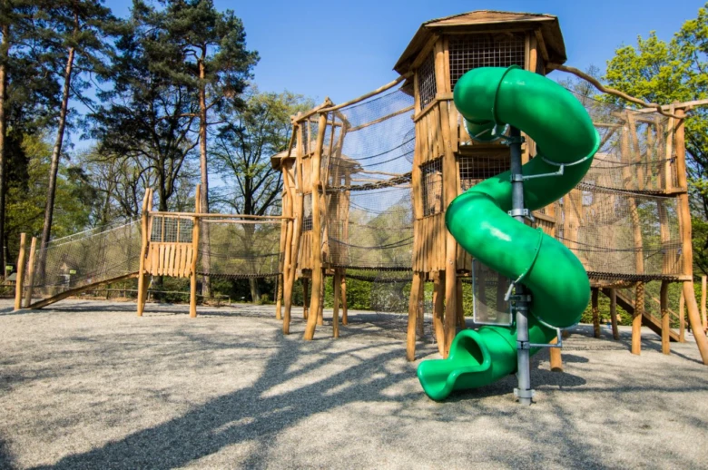 Hřiště s dřevěnou hradbou a zelenou skluzavkou v botanickém parku Ostrava.