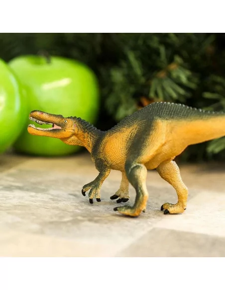 Plastová hračka dinosaura Suchomimus na dlažbě s jablky v pozadí.